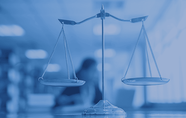 תמונת מאזניים מונחים על שולחן כשמאחור במטושטש יושב איש עסקים מול מחשב